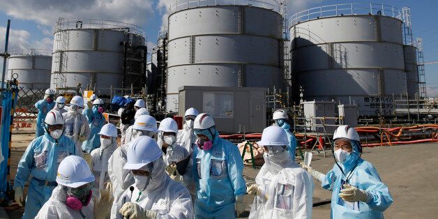 FILE - In this Feb. 10, 2016, file photo, members of a media tour group wearing a protective suit and a mask walk together after they receive a briefing from Tokyo Electric Power Co. employees (in blue) in front of storage tanks for radioactive water at the tsunami-crippled Fukushima Dai-ichi nuclear power plant in Okuma, Fukushima Prefecture, northeastern Japan. In an AP interview, a chief architect of an âice wallâ being built into the ground around the broken Fukushima nuclear plant defends the project but acknowledges it wonât be watertight, and as much as 50 tons of radiated water will still accumulate each day. TEPCO, the utility that operates the facility, resorted to the $312 million frozen barrier after it became clear that something had to be done to stem the flow of water into and out of the broken reactors so that they can be dismantled. (Toru Hanai/Pool Photo via AP, File)