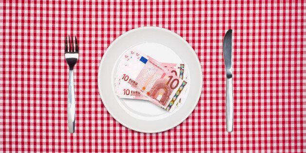 Ten Euro notes on a white dinner plate with knife and fork on a red checked tablecloth. Cost of food or restaurant concept. Overhead view.