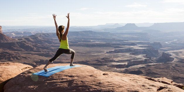 A young woman practicing yoga on top of a cliff at sunset.