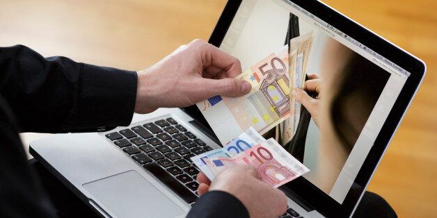BERLIN, GERMANY - NOVEMBER 21: In this photo illustration a man holds a fifty euro note in front of a computer screen that displays a purse filled with money on November 21, 2013, in Berlin, Germany. The picture symbolizes online money. (Photo illustration gby Thomas Imo/Photothek via Getty Images)