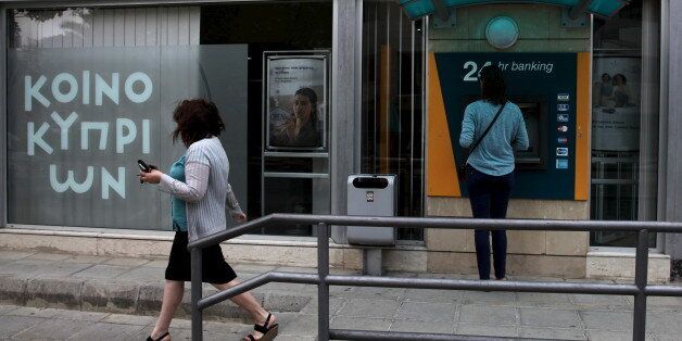 A woman withdraw money from ATMs at a branch of the Bank of Cyprus while another one pass by in Nicosia May 29, 2015.The Bank of Cyprus, the island's largest lender, was scheduled to release its first-quarter results on May 29, 2015. REUTERS/Yiannis Kourtoglou