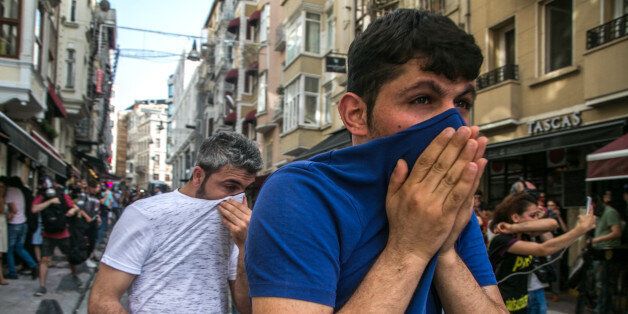 People cover their face with t-shirts as Turkish anti-riot police officers fire rubber bullets to disperse demonstrators gathered for a rally staged by the LGBT community on Istiklal avenue in Istanbul on June 19, 2016.Turkish riot police fired rubber bullets and tear gas to break up a rally staged by the LGBT community in Istanbul on June 19 in defiance of a ban. Several hundred police surrounded the main Taksim Square -- where all demonstrations have been banned since 2013 -- to prevent the 'Trans Pride' event taking place during Ramadan. / AFP / GURCAN OZTURK (Photo credit should read GURCAN OZTURK/AFP/Getty Images)