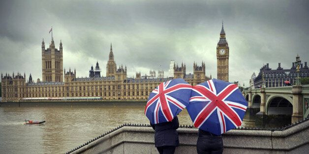 'Tourists huddle beneath British flag umbrellas (they sell them there) during a London summer rainstorm near the Houses of Parliament. A dark cloudy typical summer day!Westminster, LondonUK'