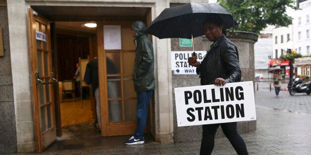 A woman carries an umbrella and a polling station sign at a polling station for the Referendum on the European Union in north London, Britain, June 23, 2016. REUTERS/Neil Hall