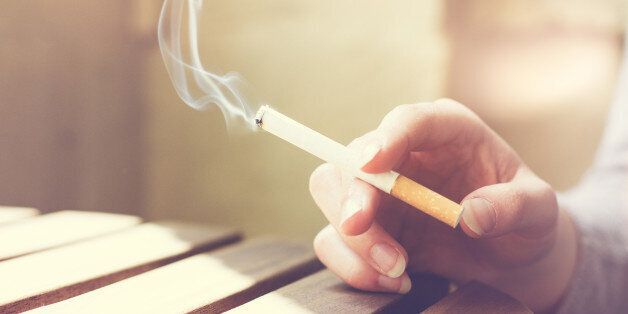 Woman smoker smoking a filter tip cigarette with her hand resting on a slatted wooden table with copy space, close up view