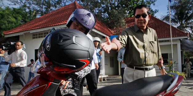 Cambodia's Prime Minister Hun Sen, right, reaches for his helmet afer paying a traffic fine at a police station in Phnom Penh, Cambodia, Friday, June 24, 2016. Cambodia's long-serving prime minister, who is known to often boast about his work and achievements, on Friday pad fine for driving a village motorbike without a helmet. (AP Photo/Heng Sinith)