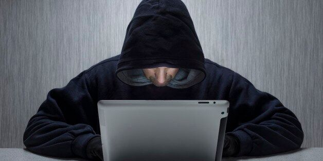 An anonymous hooded male using a tablet computer to represent a cyber criminal. (Photo by: Loop Images/UIG via Getty Images)
