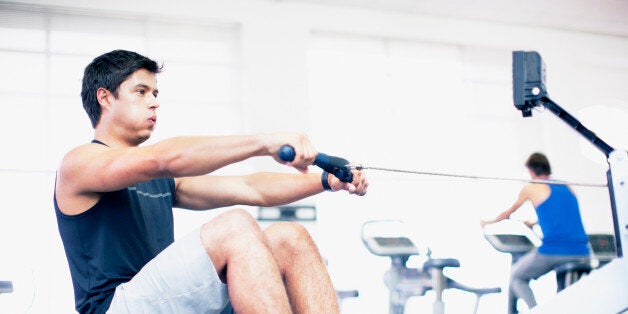 Young man exercising on rowing machine in gymnasium