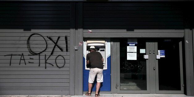 A tourist uses an ATM at a closed Attica Bank branch in Athens, Greece July 13, 2015. Euro zone leaders clinched a deal with Greece on Monday to negotiate a third bailout to keep the near-bankrupt country in the euro zone after a whole night of haggling at an emergency summit. The graffiti reads,