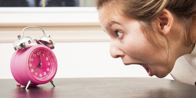 Close up as a young woman gapes at a pink alam clock in shocked panic