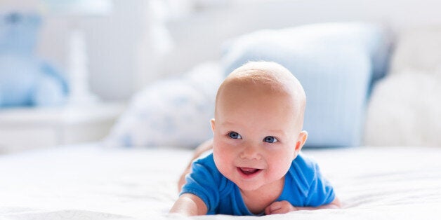 Adorable baby boy in white sunny bedroom. Newborn child relaxing in bed. Nursery for young children. Textile and bedding for kids. Family morning at home. New born kid during tummy time with toy bear.