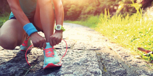 young woman runner tying shoelaces on stone trail