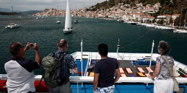 Tourists stand on the deck of a cruise ship to photograph the harbor front as they arrive at the island of Poros, Greece, on Monday, May 11, 2015. Less than three weeks after a Greek aid meeting broke up in taunts and acrimony, Finance Minister Yanis Varoufakis assured euro-area governments that his country is aiming to strike a bargain to win the final installments of its 240 billion-euro ($268 billion) aid program. Photographer: Yorgos Karahalis/Bloomberg via Getty Images