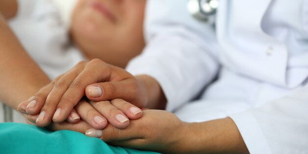 Friendly female doctor's hands holding patient's hand lying in bed for encouragement, empathy, cheering and support while medical examination. Trust and ethics concept. Bad news lessening and support