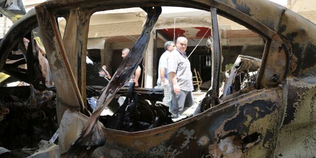 People walk past a burnt vehicle at the site of a suicide bombing suspected to have been carried out by the Islamic State (IS) group on May 22, 2016 in the Christian Wusta neighbourhood of the divided Syrian northeastern city of Qamishli. Bombings suspected to have been carried out by the Islamic State group killed at least eight people in northeastern Syria hours after a top US commander visited, security forces said. Qamishli is a mainly Kurdish city that is the de facto capital of the swathes of northern Syria where Kurdish militia have set up a self-declared autonomous administration. / AFP / DELIL SOULEIMAN (Photo credit should read DELIL SOULEIMAN/AFP/Getty Images)