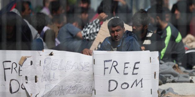 Seen through a wire fence, refugees and migrants most of them from Pakistan, hold placards during a third day of hunger strike to protest their deportation to Turkey, in the Greek island of Lesbos, Thursday, April 7, 2016. Authorities in Greece have paused deportations to Turkey and acknowledged that most migrants and refugees detained on the islands have applied for asylum. (AP Photo/Petros Giannakouris)