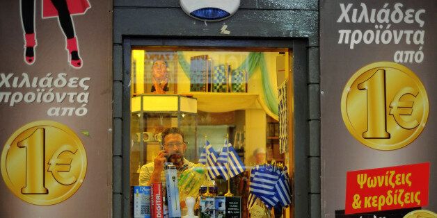 A man speaks on his mobile phone inside a discount shop that shows euro coins on the outside with slogans reading in Greek