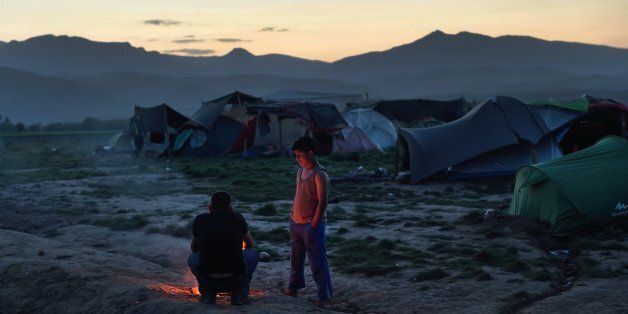 Two persons stand by a fire at a makeshift camp set by migrants and refugees at the Greek-Macedonian border near the village of Idomeni, on April 17, 2016.According to statistics released on on April 8 by the International Organization of Migrants (IOM), more than 152,000 people have arrived in Greece by sea from Turkey since January 1, nearly three-quarters of whom were Syrians. / AFP / DANIEL MIHAILESCU (Photo credit should read DANIEL MIHAILESCU/AFP/Getty Images)