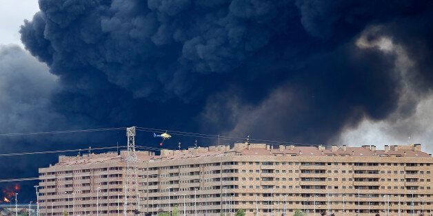 A fire fighting helicopter flies billowing black smoke rising from behind large housing blocks in Sesena, central Spain, Friday, May 13, 2016. A massive fire is raging at a sprawling tire dump in a town near Madrid, sending a spectacular cloud of thick black smoke into the air that's visible for at least 30 kilometers (20 miles). Ten teams of firefighters are trying to put out the blaze at the tire dump in the town of Sesena, still raging more than 10 hours after it started. (AP Photo/Paul White)