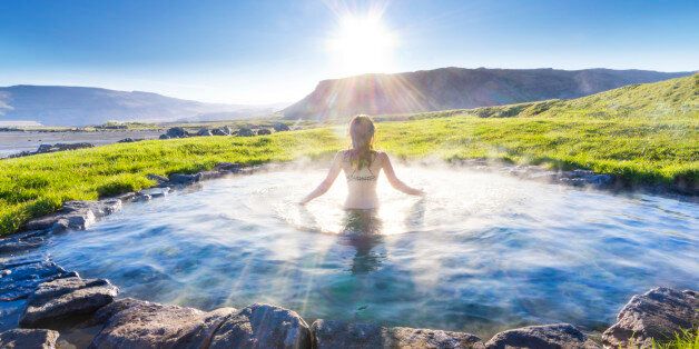 woman bathing in natural hot spring, rays of light glistening, mountains in back