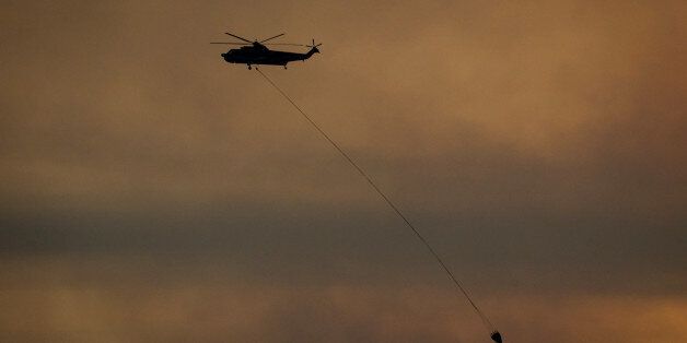 A helicopter carrying water flies during sunset in Fort McMurray, Alberta, Canada, on Friday, May 6, 2016. The wildfires ravaging Canada's oil hub in northern Alberta have rapidly spread to an area bigger than New York city, prompting the air lift of more than 8,000 evacuees as firefighters seek to salvage critical infrastructure. Photographer: Darryl Dyck/Bloomberg via Getty Images