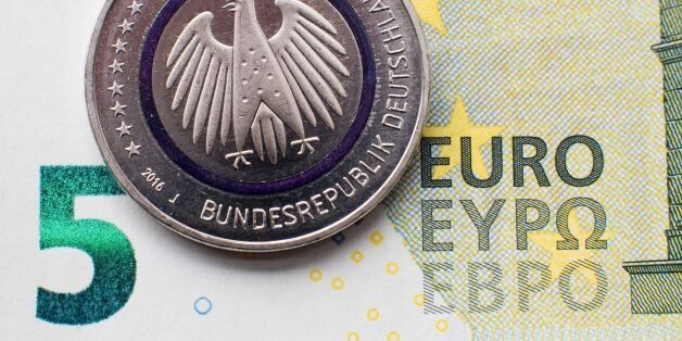 Illustration taken on April 14, 2016 in Hanover, central Germany, shows a five-euro collector coin titled 'Planet Earth' in front of a five-euro banknote.From now on, the coin is available at branches of the Deutsche Bundesbank (German Central Bank) and many other banks. As the Bundesbank explains on its internet site, 'The coin consists of three components an outer ring depicting the cosmos, with numerous planets; an inner core portraying Earth; and a blue polymer ring holding both metal components together. The polymer ring, which shines blue when held up to the light, visually represents the link between Earth and the cosmos'. / AFP / dpa / Julian Stratenschulte / Germany OUT (Photo credit should read JULIAN STRATENSCHULTE/AFP/Getty Images)