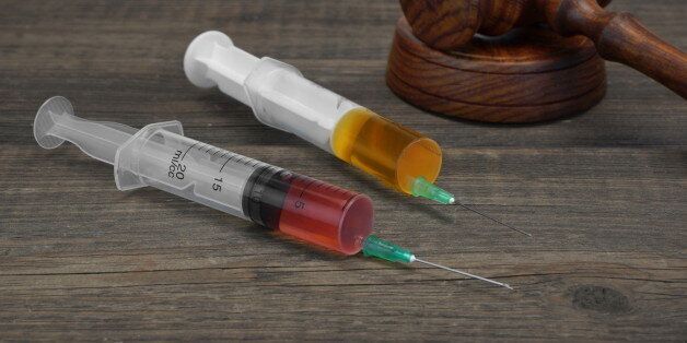 Judges Gavel And Two Medical Injection Syringes With Red And Brown Liquid On The Black Wood Background, Close-up, Top View