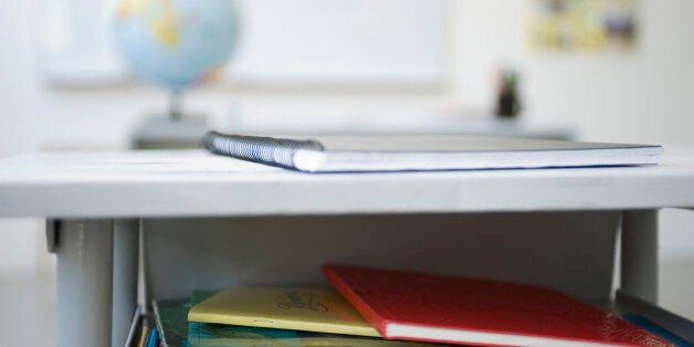 School desk containing stack of books, notebooks