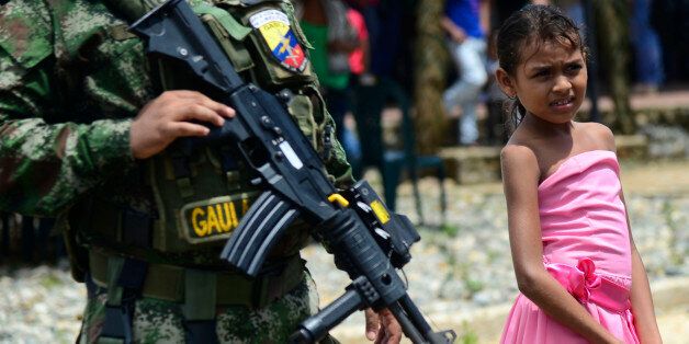 A Colombian Senu native girl stands next to soldiers during a ceremony at the new indigenous village 'Vegas de Segovia', in Zaragoza municipality, Antioquia department, Colombia on October 15, 2015. The town, built by the Colombian army for 140 indigenous families of the ethnic group Senu who have been affected by the armed conflict --especially with the National Liberation Army (ELN) guerrillas, includes a child development centre, community hall, health centre, sewerage and electricity. AFP PHOTO / RAUL ARBOLEDA / AFP / RAUL ARBOLEDA (Photo credit should read RAUL ARBOLEDA/AFP/Getty Images)