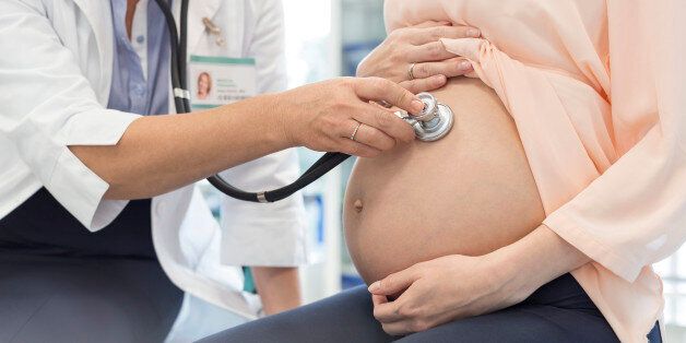 Doctor using stethoscope on pregnant patients stomach