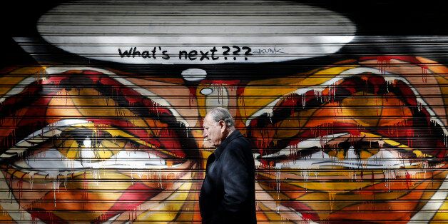 A man walks past graffiti in Athens February 25, 2015. Germany's Finance Minister Wolfgang Schaeuble said on Wednesday it had not been an easy decision for euro zone finance ministers to extend the Greek rescue plan by four months and much doubt remained about how credible Athens' latest reform commitments really were. REUTERS/Alkis Konstantinidis (GREECE - Tags: POLITICS BUSINESS TPX IMAGES OF THE DAY)