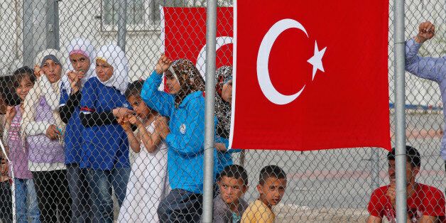 Migrants stand behind a fence at the Nizip refugee camp in Gaziantep province, southeastern Turkey, Saturday, April 23, 2016. German Chancellor Angela Merkel and top European Union officials, under pressure to reassess a migrant deportation deal with Turkey, are traveling close to Turkey's border with Syria on Saturday in a bid to bolster the troubled agreement. (AP Photo/Lefteris Pitarakis)