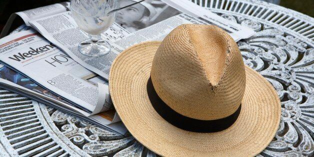 Panama hat and empty dessert bowl on top of broadsheet newspaper on caste iron garden table