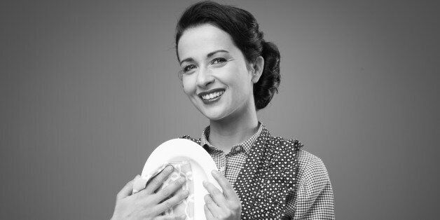 Smiling vintage housewife drying and polishing a dish with a cloth