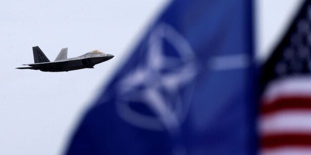 NATO and U.S. flags flutter as U.S. Air Force F-22 Raptor fighter flies over the military air base in Siauliai, Lithuania, April 27, 2016. REUTERS/Ints Kalnins TPX IMAGES OF THE DAY