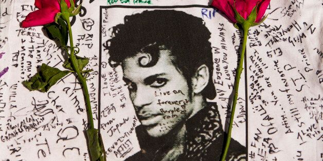 Flowers lay on a T-shirt signed by fans of singer Prince at a makeshift memorial place created outside Apollo Theater in New York, Friday, April 22, 2016. The pop star died Thursday at the age of 57. (AP Photo/Andres Kudacki)