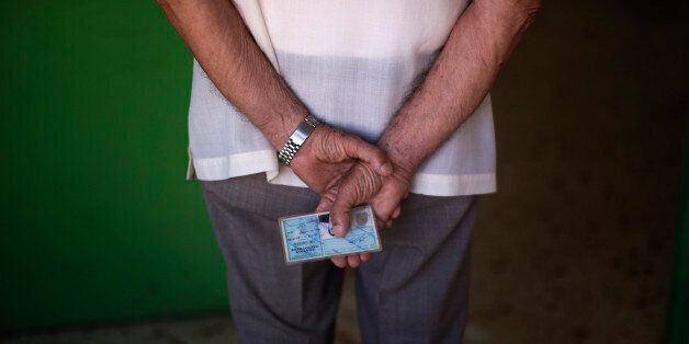 A man holds his ID card as he waits for his turn to cast his vote at a polling station in Athens, Sunday, July 5, 2015. Greeks were voting Sunday in a critical bailout referendum, with opinion polls showing people evenly split on whether to accept creditors' proposals for more austerity in exchange for rescue loans, or defiantly reject the deal. (AP Photo/Emilio Morenatti)
