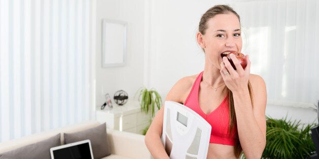cheerful young woman holding scales and eating fruit weight loss program