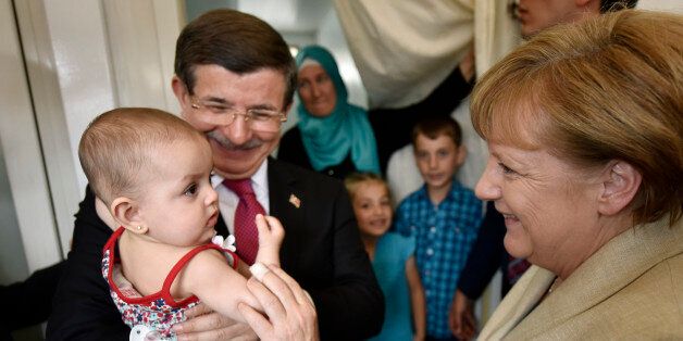 GAZIANTEP, TURKEY - APRIL 23: In this photo provided by the German Government Press Office (BPA), Turkey's Prime Minister, Ahmet Davutoglu holds a child as German Chancellor Angela Merkel speaks to her in a refugee camp on April 23, 2016 in Gaziantep, Turkey. Merkel is in Germany to commence the EU aid program for Syrians in Turkey and visit a refugee camp. (Photo by Steffen Kugler - Pool/Bundesregierung via Getty Images)