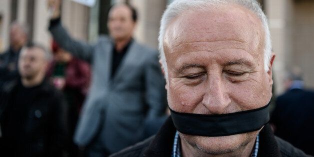 TOPSHOT - A demonstrator with his mouth covered, stands outside the Istanbul courthouse on April 1, 2016, where Turkish opposition Cumhuriyet daily's editor-in-chief Can Dundar and Ankara bureau chief Erdem Gul attend their trial.Cumhuriyet daily's editor-in-chief Can Dundar and Ankara bureau chief Erdem Gul face possible life terms on spying charges over a news report accusing President Recep Tayyip Erdogan's government of seeking to illicitly deliver arms bound for neighbouring Syria. / AFP / OZAN KOSE (Photo credit should read OZAN KOSE/AFP/Getty Images)
