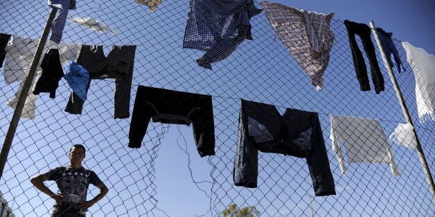 A migrant stands next to a fence with clothes left to dry, outside the main building of the disused Hellenikon Airport where stranded refugees and migrants, most of them Afghans, are temporarily accommodated in Athens, Greece, April 17, 2016. REUTERS/Michalis Karagiannis