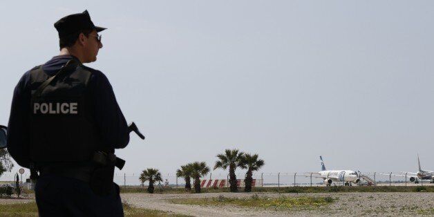 A Cypriot policeman stands guard in the vicinity of Larnaca airport where an EgyptAir Airbus A-320 (R) sits on the tarmac after being hijacked and diverted to Cyprus on March 29, 2016. / AFP / BEHROUZ MEHRI (Photo credit should read BEHROUZ MEHRI/AFP/Getty Images)