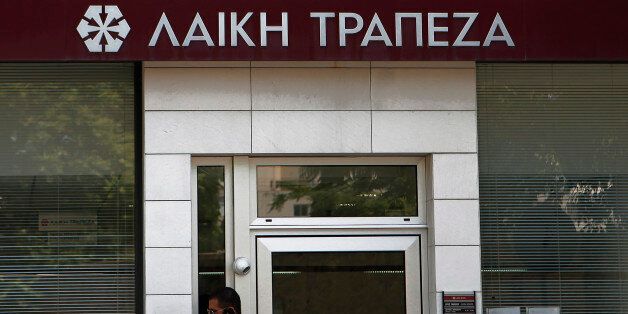 A man use his mobile phone as stands outside of a branch of Laiki Bank in central capital Nicosia, Cyprus, Tuesday, May 21, 2013. Laiki bank, which took huge losses from Greeceâs debt restructuring, is being wound down and folded into Cyprusâ largest lender, Bank of Cyprus. The move is part of a 23 billion euro financial rescue deal that Cyprus agreed in March with its euro area partners and the International Monetary Fund. The agreement also stipulates that Cyprus must raise 13 billion euros on its own to recapitalize its banks by forcing savers with over 100,000 euros in their Laiki and Bank of Cyprus accounts to take significant losses. (AP Photo/Petros Karadjias)