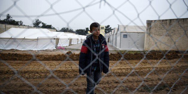 A boy stands behind a fence after the arrival of refugees and migrants at a transit center in the village of Diavata, west of the northern Greek city of Thessaloniki, Wednesday, Feb. 24, 2016. Greece has opened the second army-built transit camp in the north of the country to cope with a border bottleneck of migrants and refugees. About 1,000 asylum-seekers from Syria and Iraq were taken by bus from the border to the camp outside the northern city of Thessaloniki, police said. (AP Photo/Giannis Papanikos)