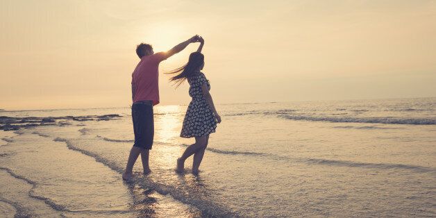 Young couple dancing on beach under sunset.