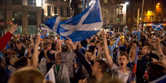 Supporters of the Yes campaign in the Scottish independence referendum cheer with Scottish Saltire flags as they await the result after the polls closed, in George Square, Glasgow, Scotland, late Thursday, Sept. 18, 2014. From the capital of Edinburgh to the far-flung Shetland Islands, Scots embraced a historic moment - and the rest of the United Kingdom held its breath - after voters turned out in unprecedented numbers for an independence referendum that could end the country's 307-year union with England. (AP Photo/Matt Dunham)
