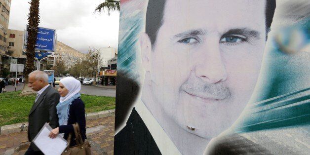 Syrians walk past a large billboard depicting a portrait of Syrian President Bashar al-Assad in the capital Damascus, on March 15, 2016. / AFP / LOUAI BESHARA (Photo credit should read LOUAI BESHARA/AFP/Getty Images)