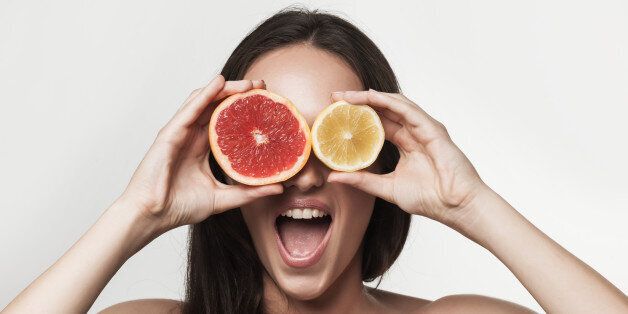 Funny portrait of young brunette woman holding fresh lemon and grapefruit. Healthy eating lifestyle and weight loss concept. Studio white background.
