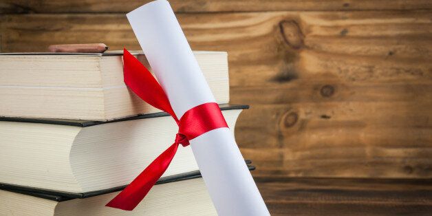 A parchment diploma scroll, rolled up with red ribbon beside a stack of books on wood background
