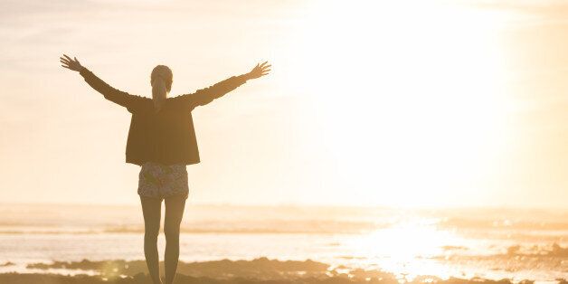 Silhouette of free woman enjoying freedom feeling happy at beach at sunset. Serene relaxing woman in pure happiness and elated enjoyment with arms raised outstretched up.
